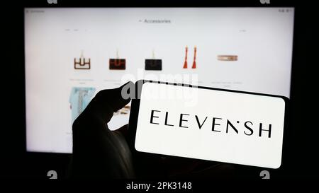 Person, die ein Mobiltelefon mit dem Logo des E-Commerce-Unternehmens ELEVENiSH auf dem Bildschirm vor der geschäftlichen Webseite hält. Konzentrieren Sie sich auf das Display des Telefons. Stockfoto
