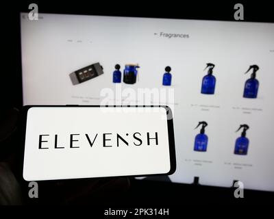 Person, die ein Mobiltelefon mit dem Logo des E-Commerce-Unternehmens ELEVENiSH auf dem Bildschirm vor der Unternehmenswebseite hält. Konzentrieren Sie sich auf das Display des Telefons. Stockfoto