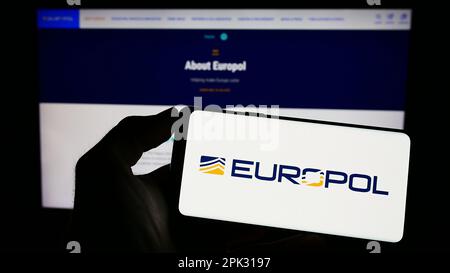 Person, die ein Mobiltelefon mit dem Logo der EU-Strafverfolgungsbehörde Europol auf dem Bildschirm vor der Webseite hält. Konzentrieren Sie sich auf das Display des Telefons. Stockfoto
