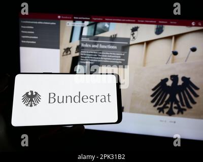 Person, die ein Mobiltelefon mit dem Siegel des deutschen Bundesrats auf dem Bildschirm vor der Webseite hält. Konzentrieren Sie sich auf das Display des Telefons. Stockfoto