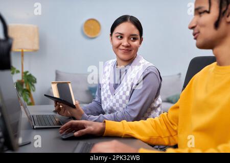 Porträt einer jungen Frau, die einen männlichen Kollegen anlächelt, während sie gemeinsam an einem Softwareentwicklungsprojekt arbeitet Stockfoto