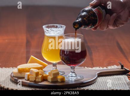 Gläser belgisches gelbes, blondes und dunkelbraunes Bier, hergestellt in Abbey und Holzbrett mit einer Vielzahl belgischer Käsesorten, Speisen und Bier in Belgien Stockfoto