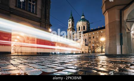 Leichte Straßenbahn zwischen historischen Gebäuden bei Nacht. Nasse Kopfsteinpflaster in der Kleinseite in Prag, Tschechische Republik. Stockfoto