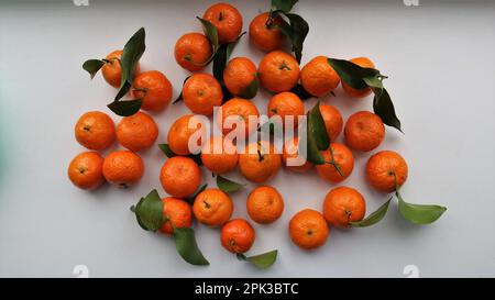 Eine Gruppe heller Mandarinen mit Blättern auf einer hellen Oberfläche, Zitrusfrüchte auf einem weißen Tisch als Mandarinenhintergrund Stockfoto