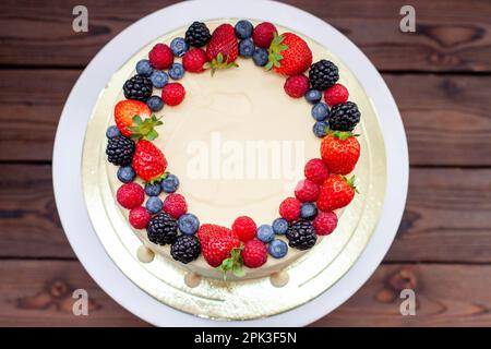 Käsekuchen mit frischen Erdbeeren, Himbeeren, Heidelbeeren und Brombeeren, geschmolzener weißer Schokolade auf rustikalem Holzkakestand und Hintergrund Stockfoto