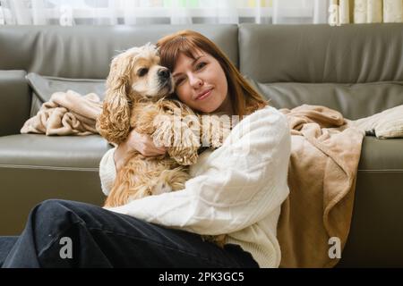 Die süße junge weisse Gastgeberin streichelt den amerikanischen Cockerspaniel und drückt ihr Gesicht gegen ihn. Familienkonzept Stockfoto