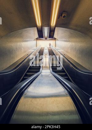 Ein einsamer Mann, der auf einer U-Bahn-Rolltreppe rausklettert. Symmetrische unterirdische bewegliche Treppe Stockfoto