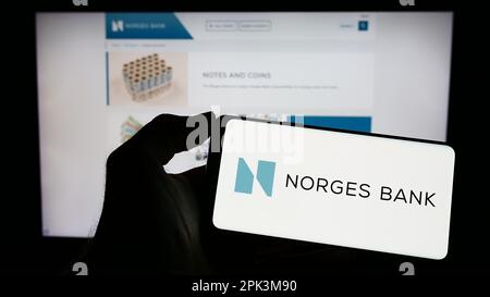 Person, die ein Handy mit dem Logo der norwegischen Zentralbank Norges Bank auf dem Bildschirm vor der Webseite hält. Konzentrieren Sie sich auf das Display des Telefons. Stockfoto