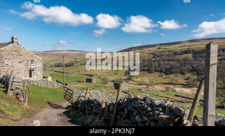 Atemberaubende Aussicht vorbei an einem Bauernhaus und durch ein offenes Tor entlang Swaledale zu alten Steinscheunen mit einem Wegweiser nach Keld, Yorkshire Dales National Stockfoto