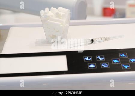 Verschließen Sie die Nadelspritze und die Mundwoll auf dem Zahnarztpflaster. Selektiver Verschluss von Nadel und Baumwolle. Offener Raum. Stockfoto