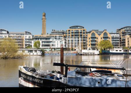 Hausboote auf einer ruhigen Themse mit Kew Bridge Road im hinteren Teil mit dem viktorianischen Standrohrturm Museum of Water & Steam Stockfoto