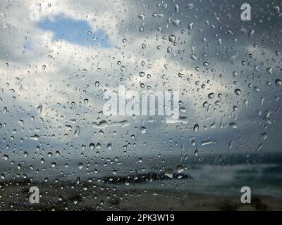 Regentropfen auf dem Autofenster. Nahaufnahme auf grauem Hintergrund. Stockfoto