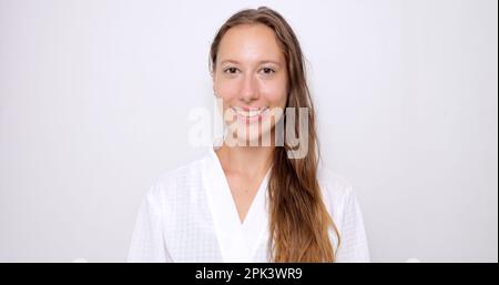 Porträt einer jungen Frau mit langen Haaren im weißen Bademantel, die lächelt Stockfoto
