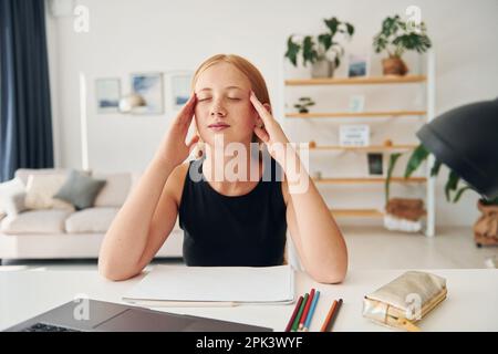 Ich habe Kopfschmerzen. Eine Teenagerin mit blondem Haar ist tagsüber zu Hause Stockfoto