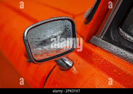 Rückspiegel eines orangefarbenen Retro-Autos in der Regennaht Stockfoto