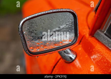 Rückspiegel eines orangefarbenen Retro-Autos in der Regennaht Stockfoto