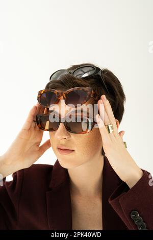 Porträt einer trendigen Frau, die verschiedene modische Sonnenbrillen trägt, isoliert auf grauem Stockbild Stockfoto