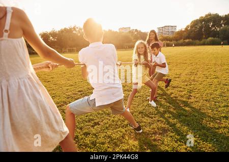 Sie spielen Tauziehen. Die Gruppe glücklicher Kinder ist tagsüber draußen auf dem Sportplatz Stockfoto