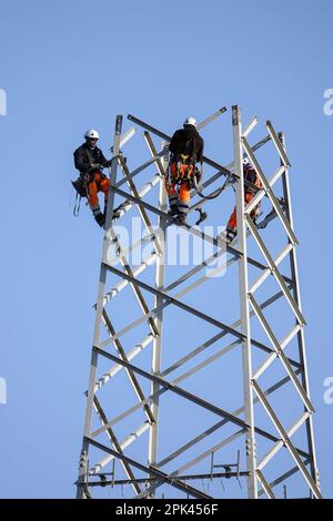 Elektriker arbeiten über Kopf, um einen Hochspannungspylon zum Austausch zu zerlegen. Mailand, Italien - April 2023 Stockfoto