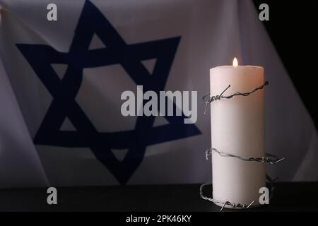 Israelische Flagge, Stacheldraht und brennende Kerze auf schwarzem Hintergrund. Holocaust-Gedächtnisfeiertag Stockfoto