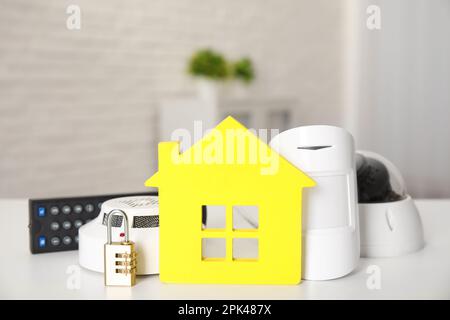 Hausmodell, CCTV-Kamera, Schloss, Fernbedienung, Rauch- und Bewegungsmelder auf dem Tisch im Raum. Heim-Sicherheitssystem Stockfoto