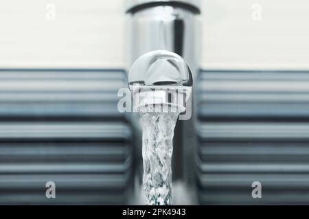 Wasser fließt aus dem Hahn auf verschwommenem Hintergrund, Nahaufnahme Stockfoto