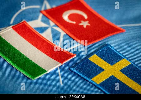 Türkische und ungarische Flaggen vor dem Hintergrund des NATO-Symbols, schwedische Flagge gegenüber, Konzept, schwierige Verhandlungen und Widerstand gegen die Werbung Stockfoto