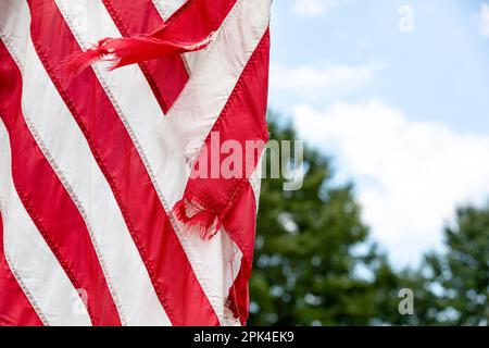 Alte, zerrissene und zerrissene amerikanische Flagge, die draußen fliegt. Patriotisches und politisches Konzept. Stockfoto