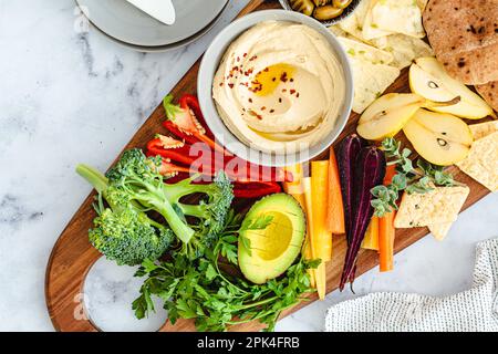 Vegetarisches Snackboard mit Hummus, Gemüse, Obst, Oliven, Pita und Crackern. Gesundes Essen, vegane Ernährung, Partykonzept. Stockfoto