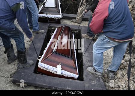 Kommunale Arbeiter heben die Särge während der Beerdigung ukrainischer Soldaten in Gräber Stockfoto