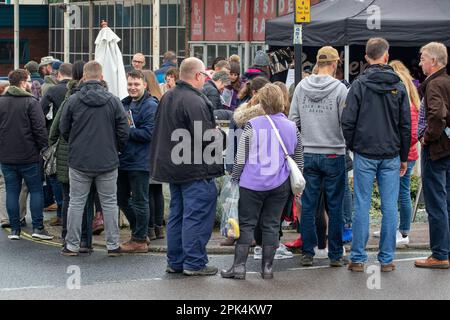 Kunden, die sich mit der britischen Besessenheit beschäftigen, sich bei dieser Gelegenheit in der Schlange zu stellen, um ein kleines Stück Wurst zu bekommen, das nicht umsonst ist Stockfoto