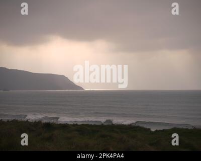 Während des Sturms Ophelia am 15. Oktober 2017 erstrahlt die Sonne hinter organischen Sturmwolken, um die Küste an der Widemouth Bay in Cornwall zu erleuchten Stockfoto