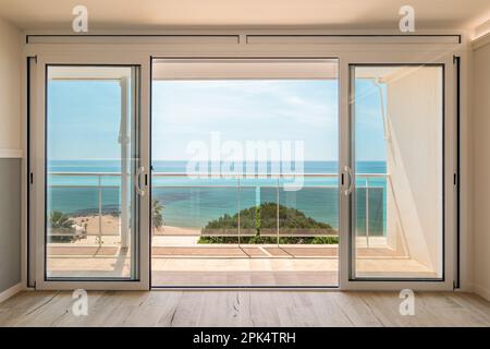 Malerischer Blick von einem Gästehaus durch Panoramafenster mit Terrasse auf das Meer an einem sonnigen, warmen Sommertag mit blauem Himmel in einem Luxusresort Stockfoto