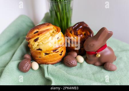 Hausgemachtes traditionelles Ostergebäck liegt auf einer grünen Serviette mit einem Blumenstrauß, einem Kaninchen und Schokoladeneiern. Osterbacken und Dekoration Stockfoto