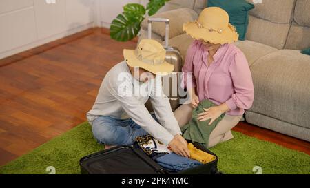 Asiatisches Seniorenpaar packt Kleidung und so für eine gemeinsame Reise zu Hause Stockfoto