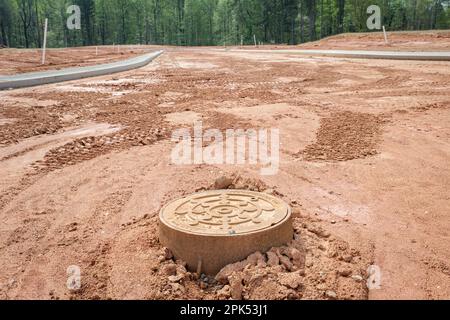 Die Eisenmanlochabdeckung in der Straße im Neubau von Unterteilungen Stockfoto