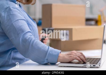 Nahaufnahme Laptop prüft Bestellungen und scannt den Barcode auf Paketen für den Versand. Online-Marktplatz, Stockfoto