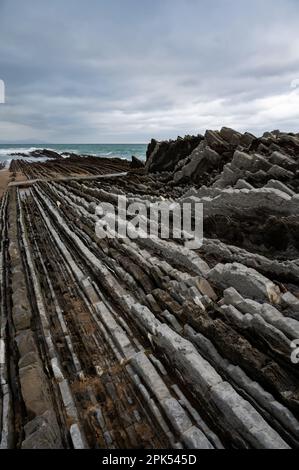 Blick auf steil geneigte Schichten von Flysch-geologischer Formation an der Atlantikküste bei Zumaia bei Ebbe, Baskenland, Spanien Stockfoto