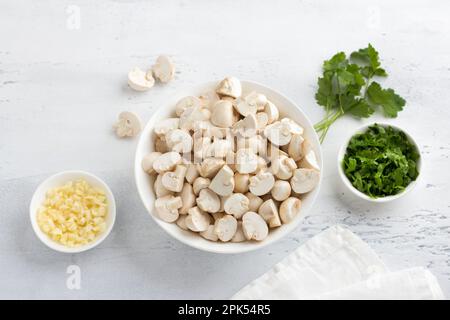 Frisch gehackter Mini-Champignon, gehackter Knoblauch und Petersilie, Zutaten auf einem hellgrauen Tisch, hausgemachtes Essen, Draufsicht Stockfoto