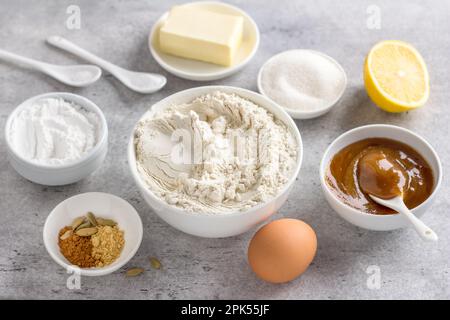 Zutaten für die Zubereitung von gedämpftem Honig-Lebkuchen: Weizenmehl, Honig, Ei, Butter, Zucker, Puderzucker, Zitrone, Backpulver, Gewürze, auf einem grauen Rücken Stockfoto