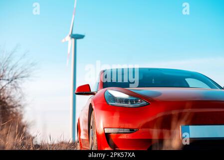 Blick auf ein geparktes rotes Elektroauto. Windturbine im Hintergrund Stockfoto