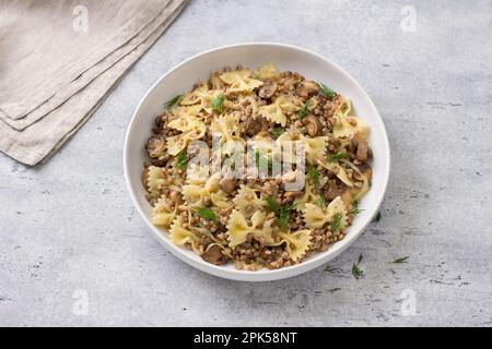 Traditionelles jüdisches Gericht Kasha Varnishkes: Buchweizen, Pasta, Champignon-Pilze, gebratene Zwiebeln mit Kräutern auf grauem, strukturiertem Hintergrund, Draufsicht Stockfoto