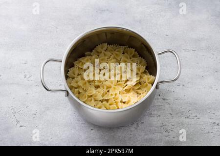 Metallpfanne mit gekochter Farfalle-Pasta, traditionelle italienische Speisen, hausgemachte einfache Speisen, auf grauem, strukturiertem Betonhintergrund, Draufsicht Stockfoto