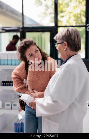Drogeriearbeiter, der einem kranken erwachsenen Klienten mit Bauchkrämpfen hilft, indem er Magenschmerzen medikamentiert, während er in der Apotheke arbeitet. Kunde mit Gastritis, der nach Pillen sucht, um Lebensmittelvergiftung zu heilen Stockfoto