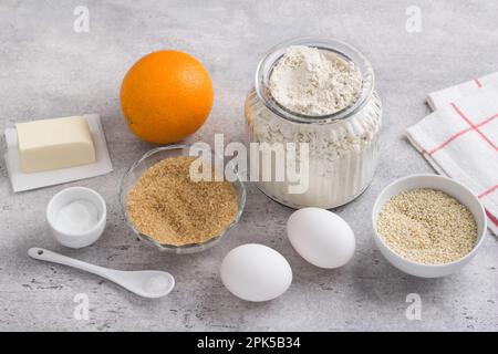 Zutaten zum Backen von Orangen-Sesamkeksen (Koulourakya oder andere): Mehl, brauner Zucker, Orangen, Sesamsamen, Eier, Butter, Salz und Backpulver drauf Stockfoto