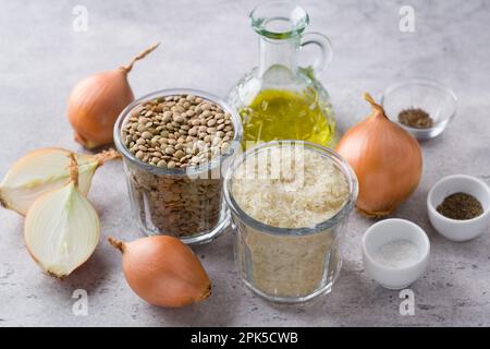 Zutaten für die Zubereitung eines traditionellen Mujadara-Gerichts aus dem Nahen Osten: Langkornreis, grüne Linsen, Zwiebeln, Olivenöl, Kreuzkümmel oder zira, Salz, schwarzer Pfeffer Stockfoto