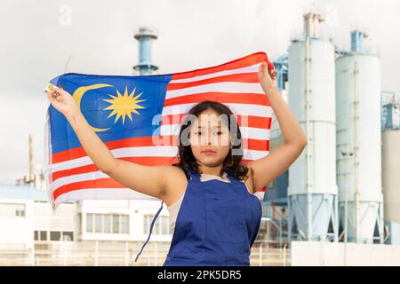 Traurige junge Frau mit der Flagge Malaysias vor dem Hintergrund der Fabrik Stockfoto