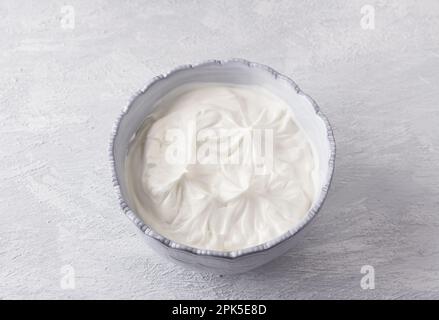 Graue Schüssel mit Schlagsahne zum Kochen des Desserts „Pavlova“ auf hellgrauem Hintergrund, Draufsicht Stockfoto
