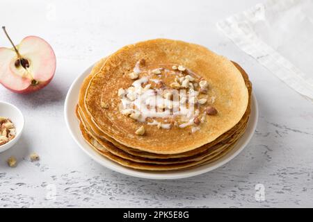 Apfelpfannkuchen mit Kondensmilch und Nüssen auf hellgrauem Hintergrund, Draufsicht. Köstliches hausgemachtes Essen Stockfoto