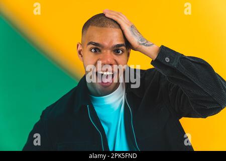 Lustiger, geschockter junger Mann mit offenem Mund, der in die Kamera schaut und seinen Kopf über gelbem Hintergrund berührt. Grüner Filter im Vordergrund. Hochwertiges Foto Stockfoto